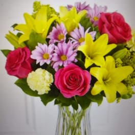 Bouquet of pink roses, yellow lilies, and lavender daisies in a clear vase