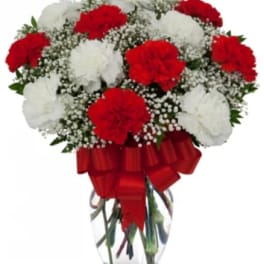 Red and white carnations in a clear glass vase with a red ribbon