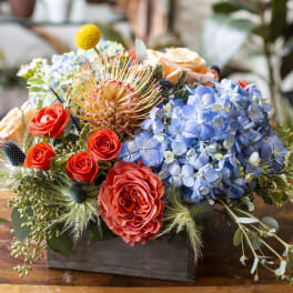 Colorful floral arrangement in a dark wooden box with roses and blue hydrangeas