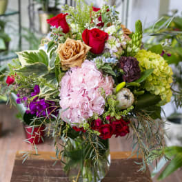 Mixed bouquet of roses, hydrangeas, and assorted blooms in a glass vase