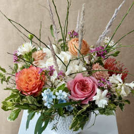 Mixed bouquet of roses, hydrangeas, and white blooms in a white vase