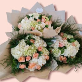Three bouquets of peach roses and white hydrangeas wrapped in kraft paper