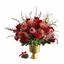 Red rose bouquet in a gold vase with a small wrapped chocolate gift