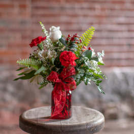 Red and white floral arrangement in a red glass vase with a ribbon