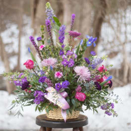 Basket arrangement of purple and pink flowers with a lavender ribbon