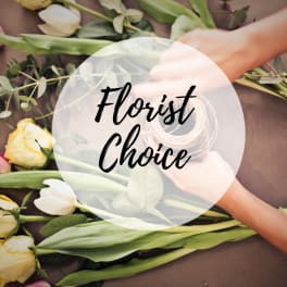 Hands arranging white and yellow tulips with greenery on a table