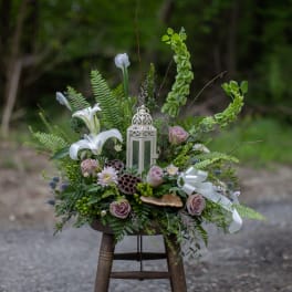 Floral arrangement with white lilies, lavender roses, and a lantern centerpiece