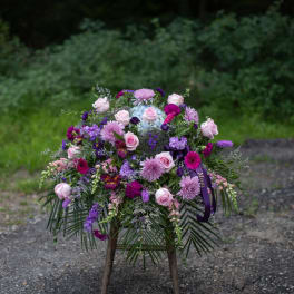 Standing floral spray with pink and purple blooms on a wooden easel