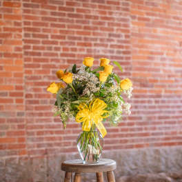 Yellow rose bouquet in a clear glass vase with a yellow ribbon