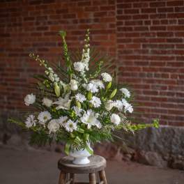 White floral arrangement in a white vase with a green ribbon
