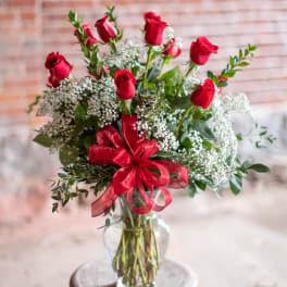 Red roses and baby's breath in a clear glass vase with a red ribbon