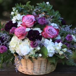 Basket arrangement of pink roses, white hydrangeas, and purple flowers