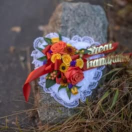 Heart-shaped floral tribute with red and yellow roses and a red ribbon