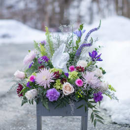 Purple and white floral arrangement in a gray container with an angel figurine