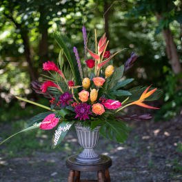 Tropical floral arrangement in a gray urn vase with bright pink and orange blooms