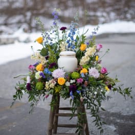Colorful floral arrangement around a white urn on a stool