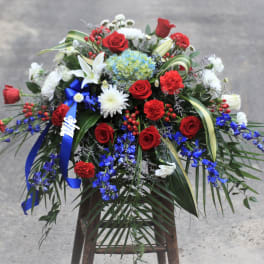 Large floral arrangement with red roses, white lilies, and blue flowers on a stand