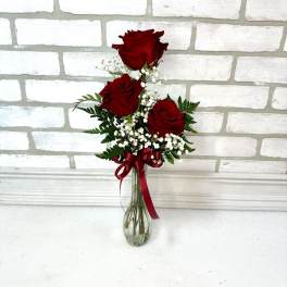 Three red roses in a clear glass vase with baby's breath and a red ribbon