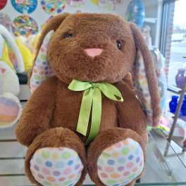 Brown plush bunny with green ribbon and pastel polka dot ears and paws on a glass shelf