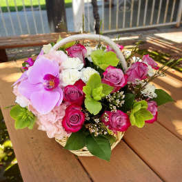 Basket arrangement of pink roses, orchids, hydrangea, and white carnations