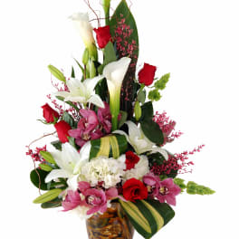 Tall bouquet of white calla lilies, red roses, and pink orchids in a glass vase