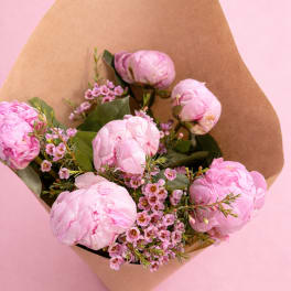 Pink peonies wrapped in brown paper with small pink filler flowers