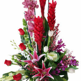Tall floral arrangement with red and pink orchids, lilies, and roses in a black vase