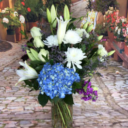Bouquet of white lilies, blue hydrangea, and white chrysanthemums in a glass vase