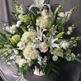 Large white floral arrangement in a basket with lilies and roses