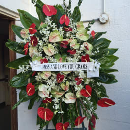 Large standing floral tribute with red and pale green blooms and a memorial ribbon