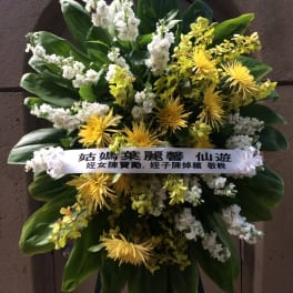 Standing floral wreath with yellow and white flowers and a condolence ribbon
