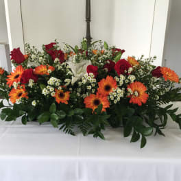 Large floral centerpiece with red roses, orange gerbera daisies, and white lilies