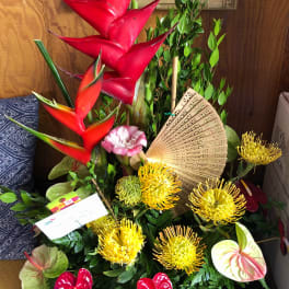 Tropical flower arrangement with red heliconia, yellow pincushion blooms, and an open fan
