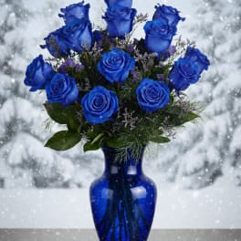 Blue roses arranged in a cobalt vase with a snowy background
