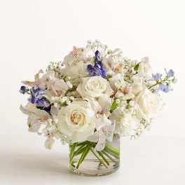 White rose bouquet with purple and pale blue flowers in a clear glass vase
