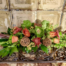 Low floral arrangement with peach roses and red blooms on a decorative metal stand