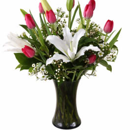 Pink tulips and white lilies arranged in a dark glass vase