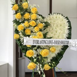 Yellow roses and white flowers arranged on a standing easel with a ribbon banner