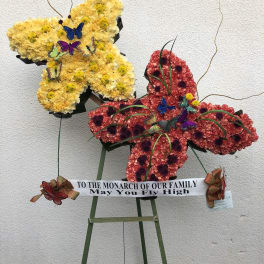 Butterfly-shaped floral display in yellow and red with a memorial ribbon