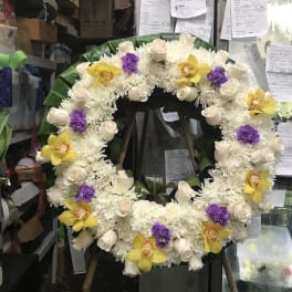Large floral wreath with white flowers, cream roses, yellow orchids, and purple accents