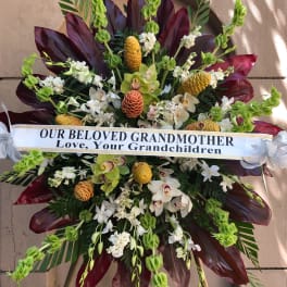 Large sympathy spray with white orchids and green blooms, accented by dark burgundy leaves