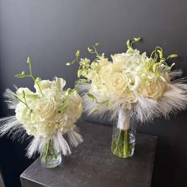 Two ivory bridal bouquets in clear glass vases with feathery accents