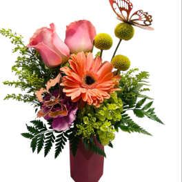 Pink roses and orange gerbera daisies in a burgundy vase with butterfly picks