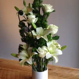 White lilies and roses arranged in a white vase with dark green accents.