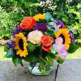 Colorful bouquet with sunflowers, roses, carnations, and alstroemeria in a glass vase