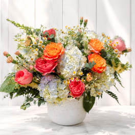 Mixed bouquet of roses, hydrangeas, and daisies in a white vase