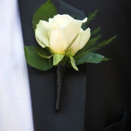 White rose boutonniere with greenery pinned to a black suit jacket