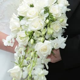 Cascading bridal bouquet of white roses and orchids held by a couple in formal attire