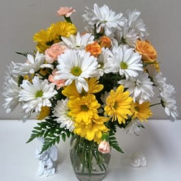 Bouquet of white and yellow daisies with peach accents in a glass vase