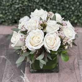 White rose bouquet in a square glass vase with small pink blossoms